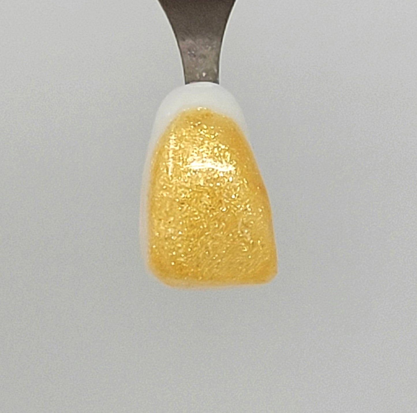 Fine Light Gold Sparkle Temporary Tattooth Colorant on a demo tooth. These colorants can be applied to teeth to temporarily alter their color or iridescence.