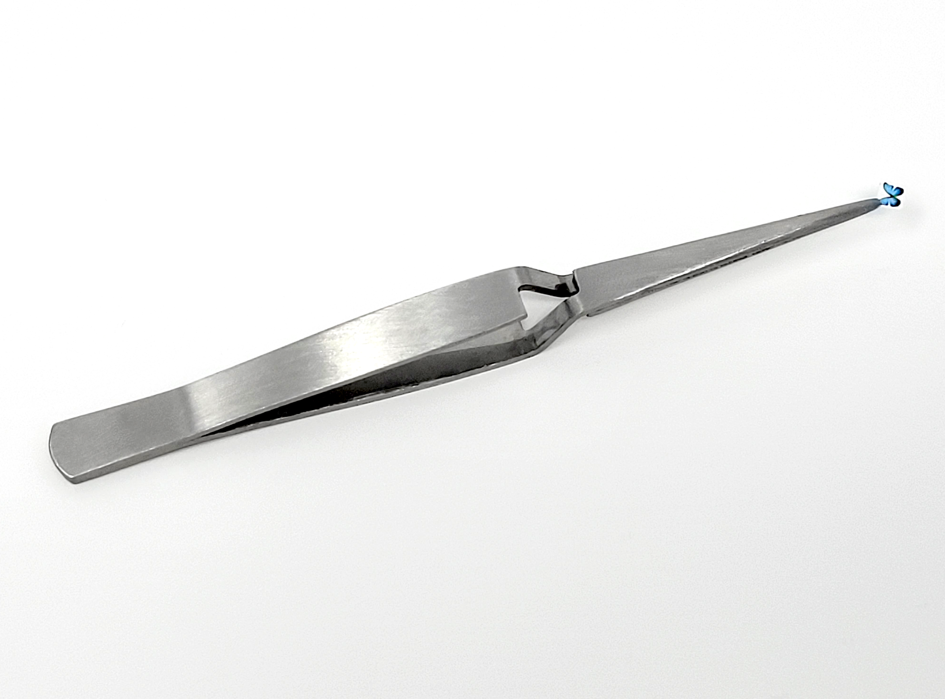 A photograph of reverse tweezers holding a pre-cut Temporary Tattooth image of a butterfly.  These reverse tweezers make applying temporary tattoos for teeth much easier.