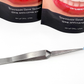 Reverse tweezers holding a trimmed Temporary Tattooth that is ready to be applied.  There are two Temporary Tattooth Home Application Kits in the background.
