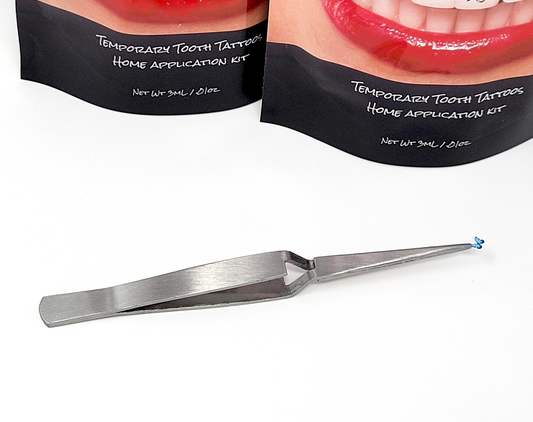 Reverse tweezers holding a trimmed Temporary Tattooth that is ready to be applied.  There are two Temporary Tattooth Home Application Kits in the background.